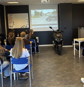 Elever på teorilektion i trafikskolans lektionssal. Framför tavlan står en moped