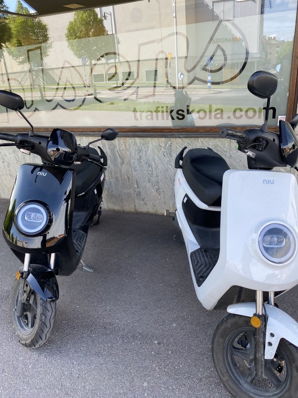 En svart och en vit elmoped parkerade framför Ahlséns skyltfönster