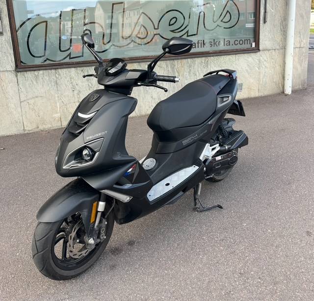 Svart moped parkerad framför Ahlséns skyltfönster