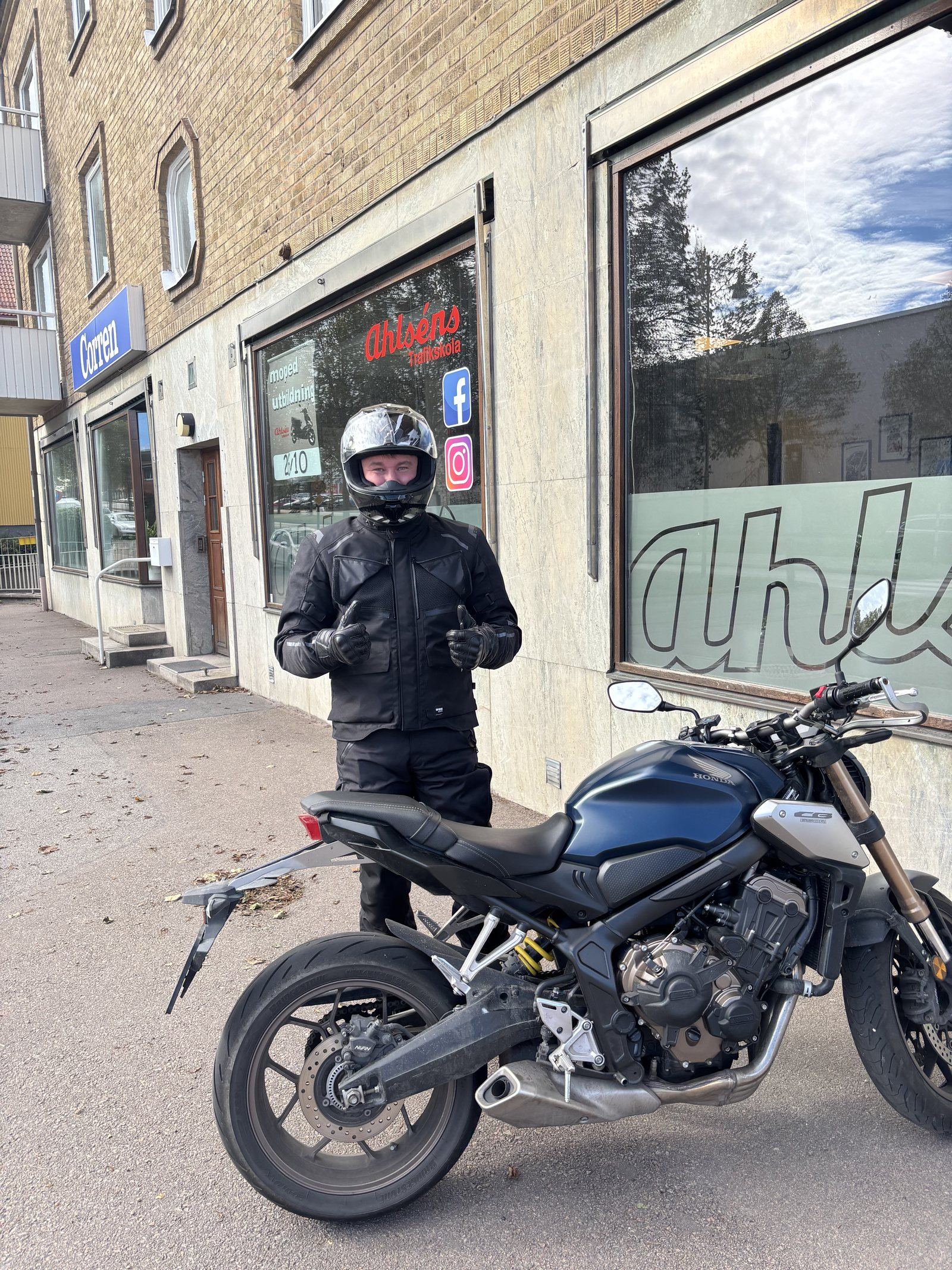 MC-elev i svart skinnställ och hjälm gör tummen upp bredvid en blå Honda-motorcykel utanför Ahlséns kontor