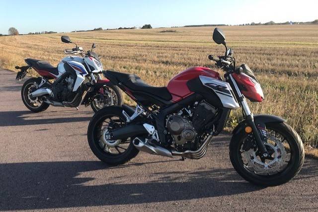 Två motorcyklar i solnedgång vid ett fält, en Honda i rött och svart och en i vitt